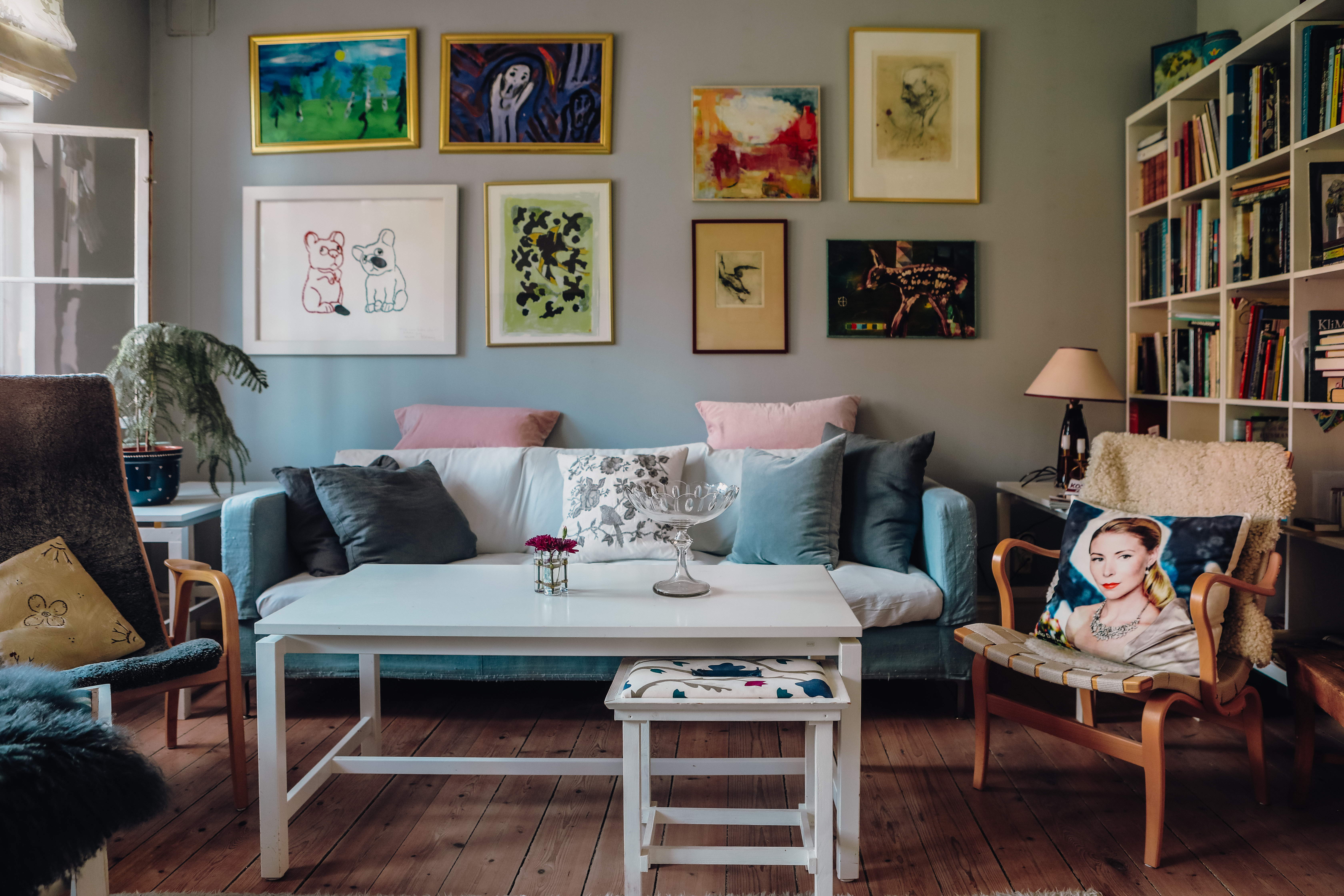 Lenas väggar är fulla av brokiga konstverk. I fåtöljen ligger en kudde prydd av ett foto av Julia. Foto: Angelica Söderberg